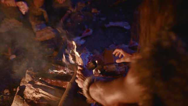 Close-up of primitive homo sapiens warming up hands and cooking animal bone on fire near cave at night. Neanderthals nomadic tribe. History of evolution.