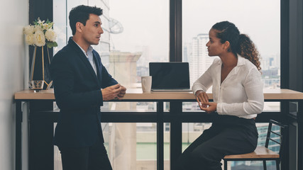 diverse business people having business conversation during coffee break time with laptop computer and cup of coffee at window corner in office