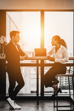 diverse business people having business conversation during coffee break time with laptop computer and cup of coffee at window corner in office