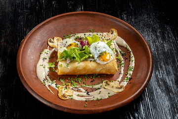 Rolled pancakes on top lies scrambled eggs. Beautiful clay plate.