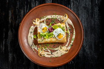 Rolled pancakes on top lies scrambled eggs. Beautiful clay plate.