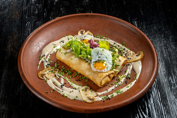 Rolled pancakes on top lies scrambled eggs. Beautiful clay plate.