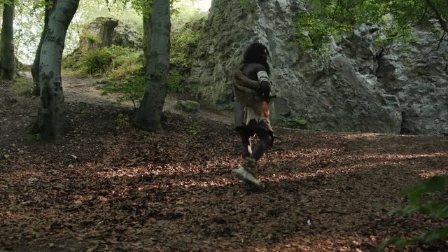 Primeval neanderthal hunter walking slowly in deep forest searching animals in slow motion. African ancestral tribesman. Homo sapiens.