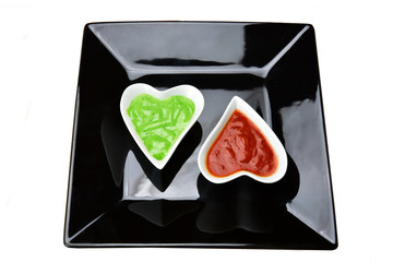 white heart shape bowl with sauces with cut breads on black background