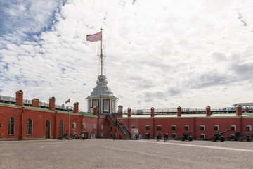 The wall and tower viewed inside the Peter and Paul Fortress in St. Petersburg, Russia, with a flag flying against the sky and cannons displaying.