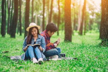 A young couple reading book and playing ukulele while sitting in the woods