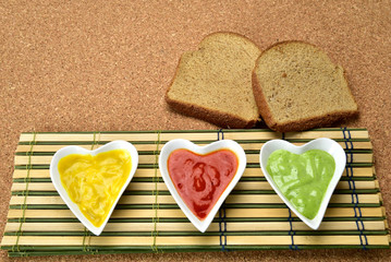 Fototapeta na wymiar white heart shape bowl with colorful sauces on cork and bamboo mat background