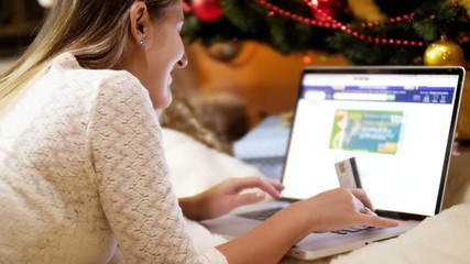 Closeup 4k footage of young woman holding credit card in hand and shopping online to order gifts and presents for Christmas. Concept shot of online shopping and e-commerce.