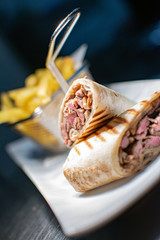 a close up shot of a grilled fillet steak tortilla wrap cooked to perfection and served with a portion of French fries