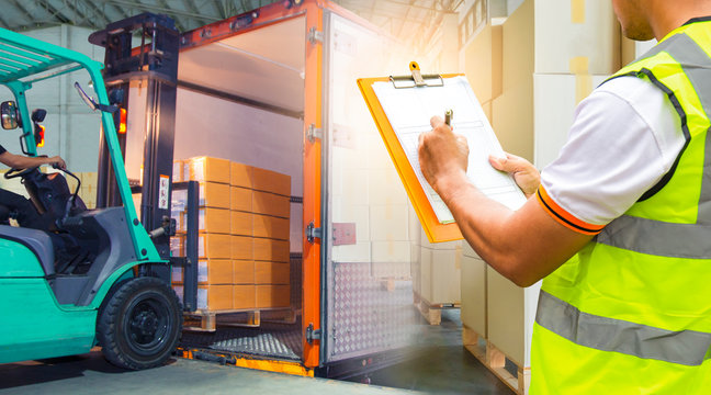 Worker Holds a Clipboard Controlling the Loading of Packaging Boxes into Shipping containers. Supply Chain. Forklift Tractor Trucks Loading at Dock Warehouse. Cargo Shipment.	