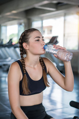 Beautiful young woman drinks water in gym. Sports nutrition concept
