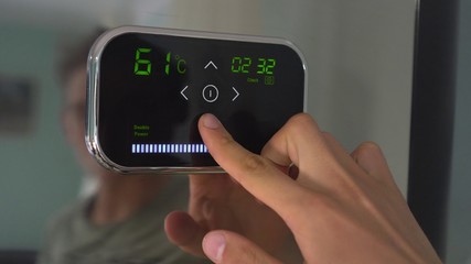 Setting a programmable room thermostat. A man adjusts the temperature on the touch panel