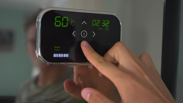 Setting a programmable room thermostat. A man adjusts the temperature on the touch panel