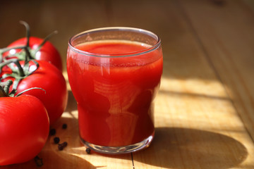 red tomato juice.  fresh tomato juice in a glass glass and ripe fruit on a light wooden Board. close up.  beautiful shadow and light.