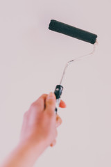 woman's hand holding paintbrush roller with dark muted blue tone against white wall