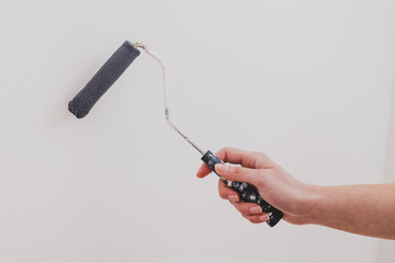 woman's hand holding paintbrush roller with dark muted blue tone against white wall