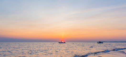 Sun sets directly above water and a boat on a perfect summer evening