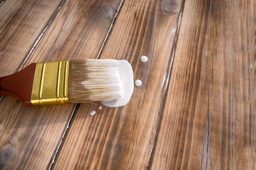 painting brush in white paint lies on a wooden textured floor close - up view from the top side