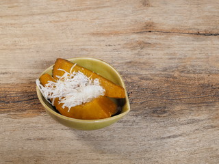 view of Khanom Fug Thong Thai dessert in a dish on wood texture background, made of steamed pumpkin mixed coconut and sugar.