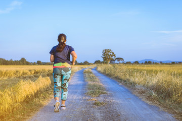 Back view of woman running and exercising on the path through the rice fields in the evening.