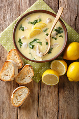 Homemade egg lemon soup with chicken and orzo pasta close-up in a bowl. Vertical top view