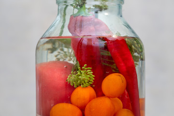 macro shot of glass jar with pickled vegetables, tomatoes, cucumbers and herbs