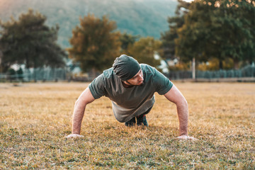 Sports and yoga. A man in sportswear push-ups during training. Park and trees on the background