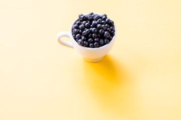 Freshly picked ripe blueberries in a cup on a table.Tasty berries. Copy space.blueberries in a small white Cup on a yellow background. Black currant harvest. Healthy food. vegetarian food