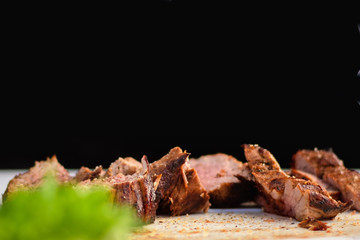 Close up of juicy grilled meat sliced on white board with black background and copy space.
