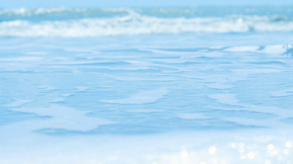 Beautiful soft wave with bubbles foams of clear blue water ocean sea on tropical sand beach blurred background , vacation holiday nature background concept.