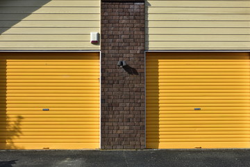 Yellow metal garage gates with brick wall between them and weatherboard cladding above.