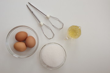Directly above shot of sugar, eggs and oil against the white background