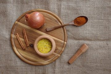 Spices in wooden bowl and wooden spoon, onion and cinnamon on the wooden cutting board. Directly above shot