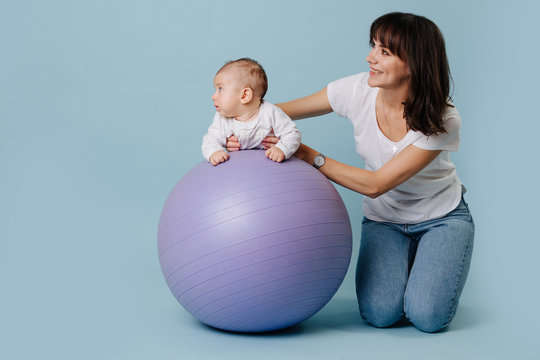 Happy Mother Doing Exercises With Her Infant Child Baby On Purple Yoga Ball