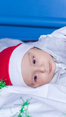 Little funny Santa boy playing with christmas or new year holiday festive garland. 1 year old baby boy in Santa Claus cap.