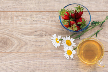 Glass cup of green tea, stawberries with white chamomile flowers on wooden background.