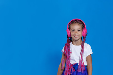 Portrait of a little sweet girl enjoying listening music by headphone, with closed eyes, isolated on blue background.