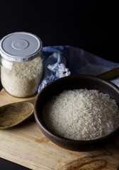 Uncooked rice in clay bowl on a wooden table with black background.