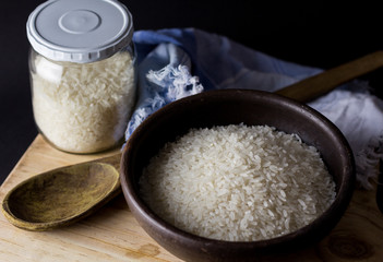 Uncooked rice in clay bowl on a wooden table with black background.