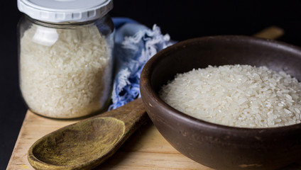 Uncooked rice in clay bowl on a wooden table with black background.