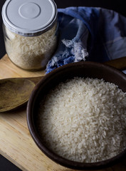 Uncooked rice in clay bowl on a wooden table with black background.