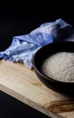Uncooked rice in clay bowl on a wooden table with black background.