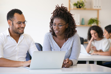 Happy diverse colleagues working on project together. Cheerful man and woman sitting at table in...