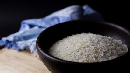 Uncooked rice in clay bowl on a wooden table with black background.