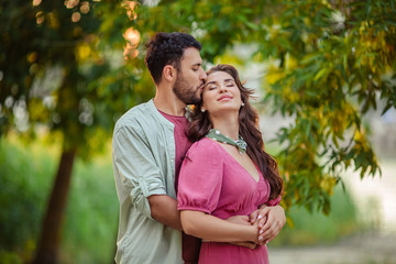 Beautiful young couple man and woman in love with each other hug and kiss on nature in the summer.