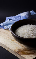 Uncooked rice in clay bowl on a wooden table with black background.