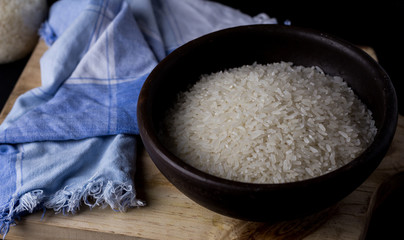 Uncooked rice in clay bowl on a wooden table with black background.