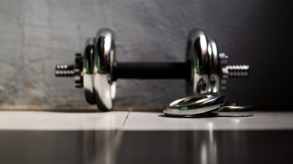 Metal dumbbell equipment with wall background rolling on the floor.