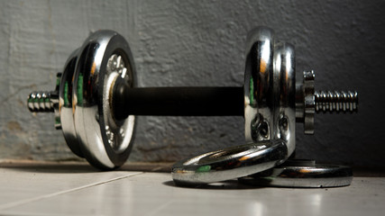 Metal dumbbell equipment with wall background rolling on the floor.