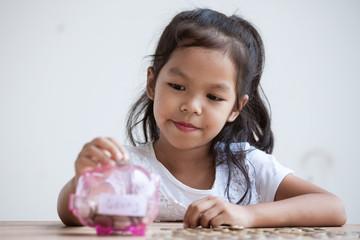 Cute asian child girl putting money into piggy bank to save money for the future